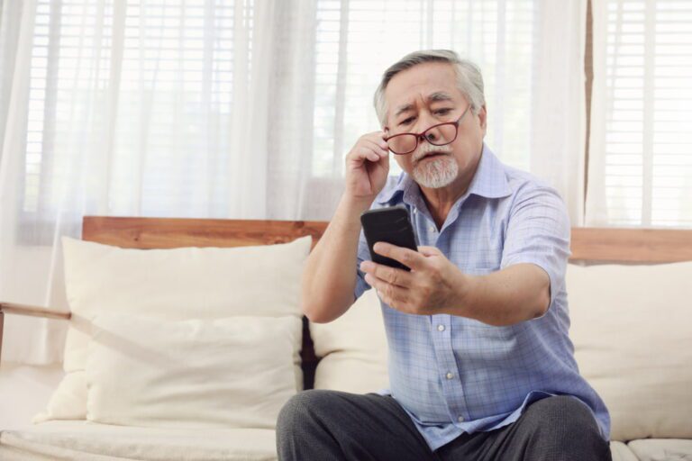 Homem idoso com dificuldade para enxergar o celular.
