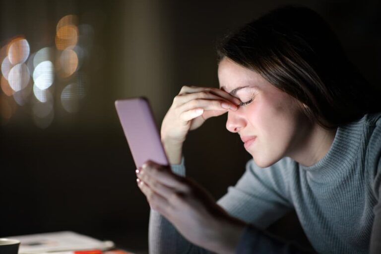 Mulher segurando o celular com dificuldade para enxergar, representando sintomas de presbiopia, como cansaço visual e dificuldade para focar objetos próximos.